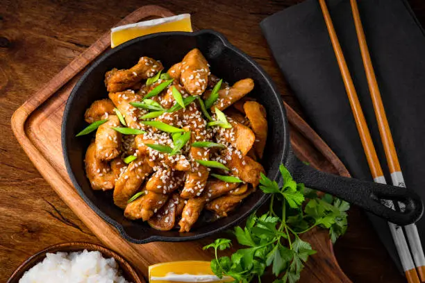 Photo of Teriyaki chicken breast in frying pan with rice and sesame seeds top view, traditional asian food