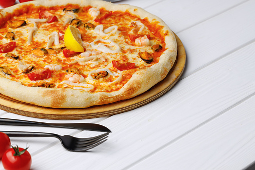 Seafood pizza on board on white wooden table close up
