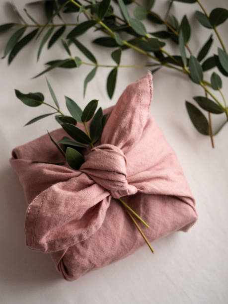 istock Gift wrapped in pink linen cloth with eucalyptus on white background 1295296418