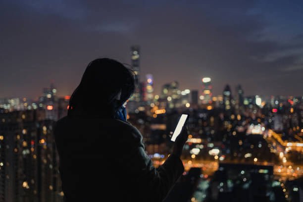Woman Using Smartphone on Skyscraper Roof at Night Woman Using Smartphone on Skyscraper Roof at Night big tech stock pictures, royalty-free photos & images