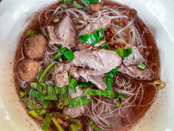 Photo of Thai Boat Noodles with bloody broth, pork, pork ball and vegetables.