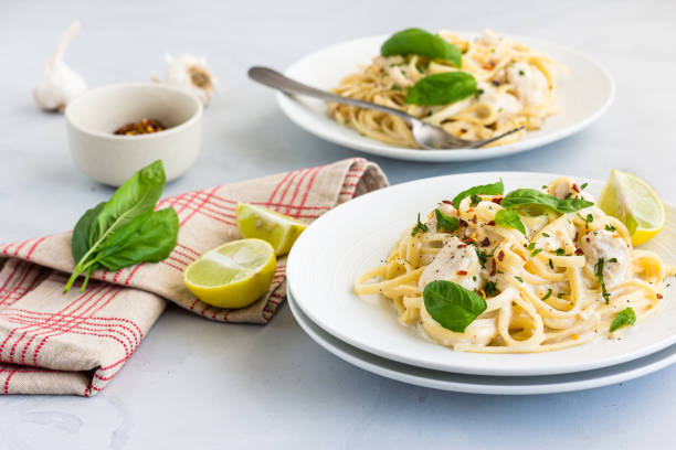 istock Linguine Pasta in White Sauce Garnished with Basil and Lemon on White Background Close-Up Photo 1295308251