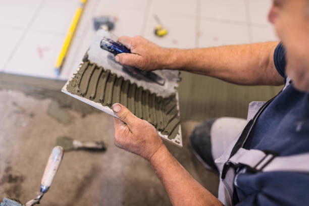 man spreads the surface of the tile with cement adhesive mass using a special hand tool - tile adhesive imagens e fotografias de stock