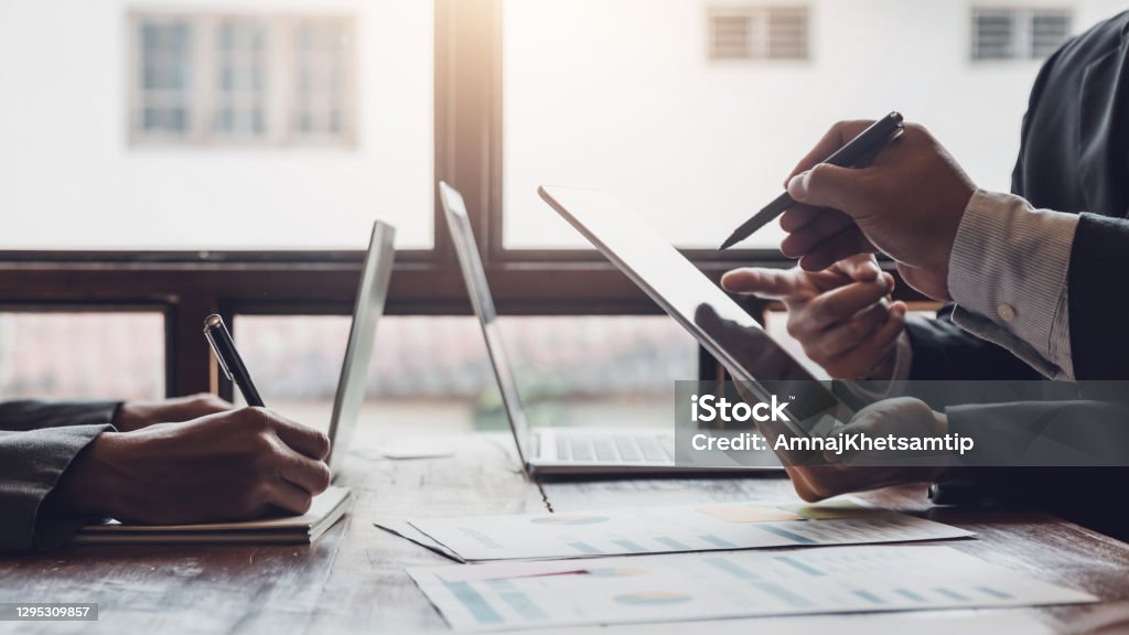 Group of business people meeting, discussing, analyzing graphs, financial data, and planning a marketing project together. Business Meeting Stock Photo