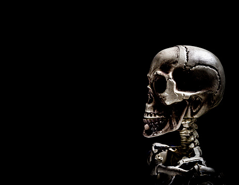 Human profile skeleton skull in dramatic low key light, corona covid-19 against pitch black background