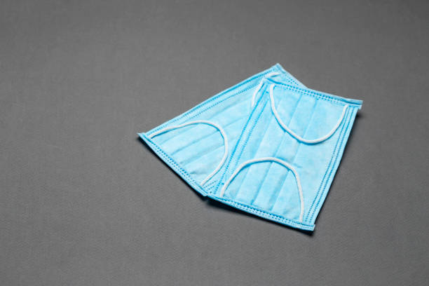 istock Surgical masks with rubber ear straps on a grey background. Typical 3-ply surgical mask to cover the mouth and nose. Procedure mask from bacteria. 1295311621