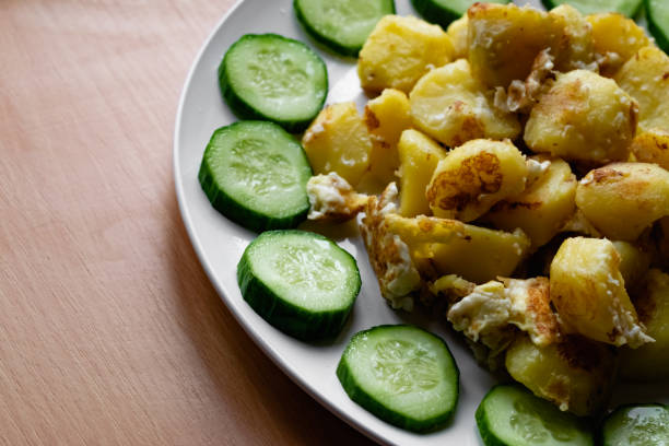 fried potato slices in a beaten egg with protein, around a circle of green juicy fresh cucumber. dish on a white plate - 11315 imagens e fotografias de stock