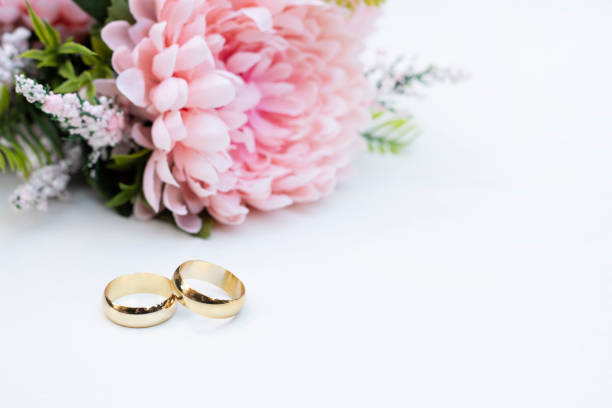 istock Pink flowers and two golden wedding rings on white background. 1295319281