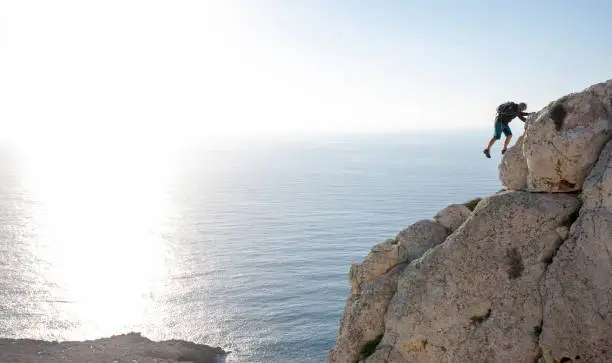 Photo of Man climbs up coastal rock in the morning