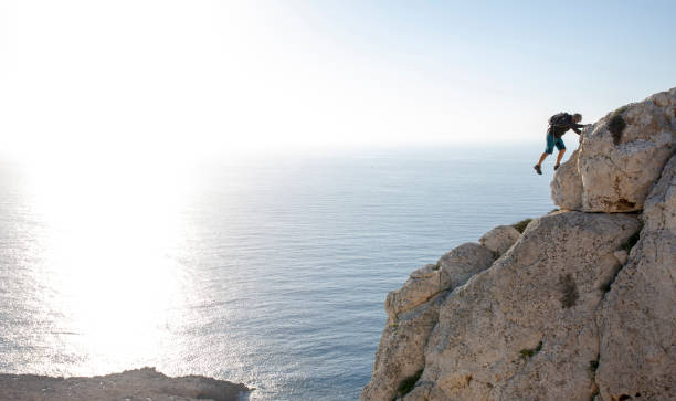 man climbs up coastal rock in the morning - climbing men sea cliff imagens e fotografias de stock