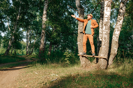 a bearded man in a hat rehearses his role in the forest, standing on a pole between the trees. acting training if not where else