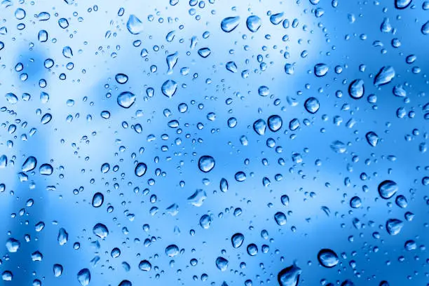 Photo of Raindrops on glass closeup. Bright beautiful background of trendy blue color. Place for text. Delicate classic backdrop. Water drop texture. Fashionable shades.