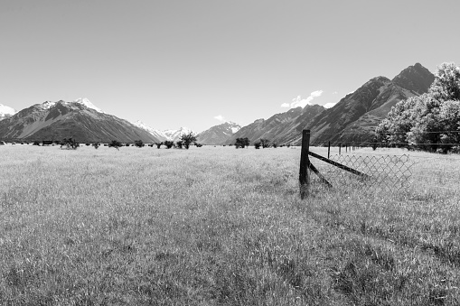 Monochrome flat farmland with fence  between Soutern Alps mountains on one of the great walks of New Zealand.