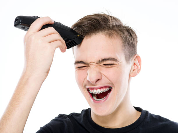 ショックを受けた10代の少年は、初めて電気��カミソリで自分の髪をカットします。若い男はかみそりで髪を切る - terrified hairdresser hairstyle color image ストックフォトと画像