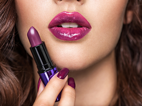 girl holds purple lipstick close to face.  Young caucasian girl doing makeup. Model. Closeup woman's portrait. Vivid make-up. Sexy female. Violet lips.