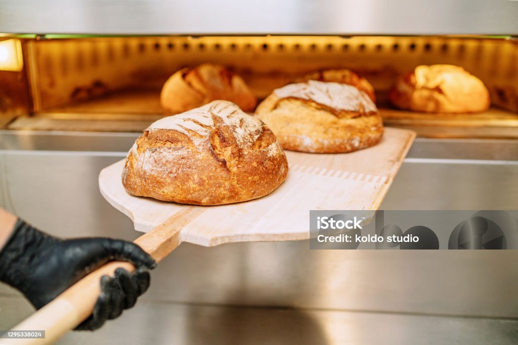 Baker putting bread in the bakery oven cowering on the floor of the bakery Bread Stock Photo