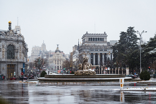 Cibeles Fountain in central Madrid under heavy snow during a snow storm in winter, with Alcala and Gran Via streets in the background.