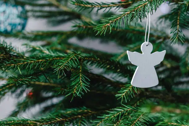 Photo of Christmas tree toy white wooden angel hanging on a spruce branch