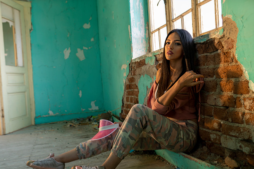 fashion portrait of young woman, in an old house, in ruin, sitting in front of an old window