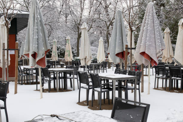 terrasse eines cafés im retiro-park mit schneebedeckten tischen und stühlen - snow park road cold stock-fotos und bilder