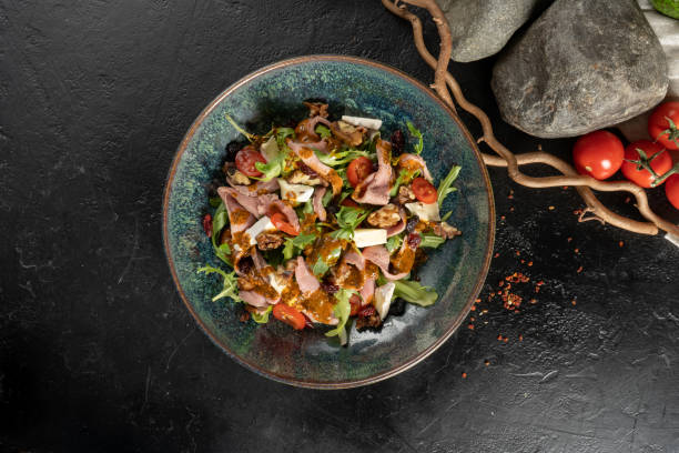 istock Salad with duck walnuts, prunes and brie cheese. Cold veggie appetizer with arugula, cherry tomatoes, poultry fillets, prunes, cheese and sun-dried tomatoes. 1295348004