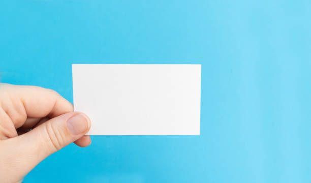 istock Hand holds a blank white business card on a blue background 1295348917