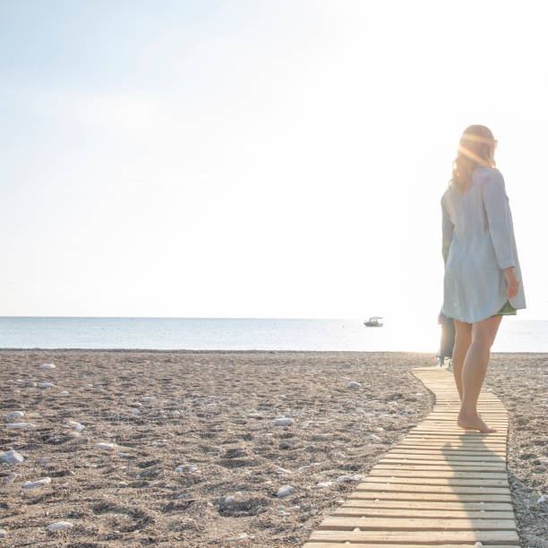 istock Woman walks down beach boarwalk in the morning 1295349130