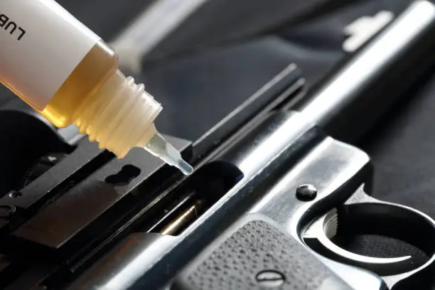 Photo of Closeup of bottle of oil lubricating a pistol. Weapon maintenance, cleaning and lubricating. CLP weapon oil S-758 / S-761.