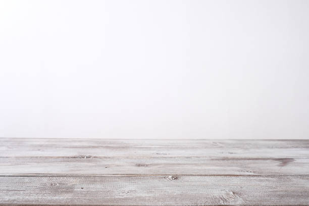 istock Empty wooden table top with a white backdrop behind, perspective background with copy space 1295353094