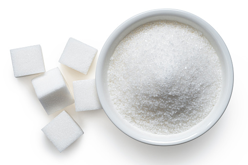 Refined granulated sugar in white ceramic bowl next to white sugar cubes isolated on white. Top view.