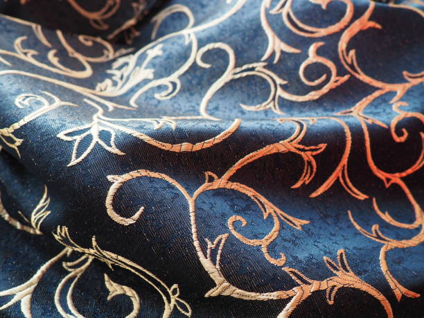 Beautiful double-sided shiny fabric of dark blue color with a golden floral pattern. Printed silk fabric, carelessly folded in waves stock photo
