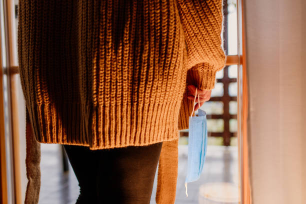 Woman holding protective mask at home Woman holding protective mask besides window at home see through leggings stock pictures, royalty-free photos & images