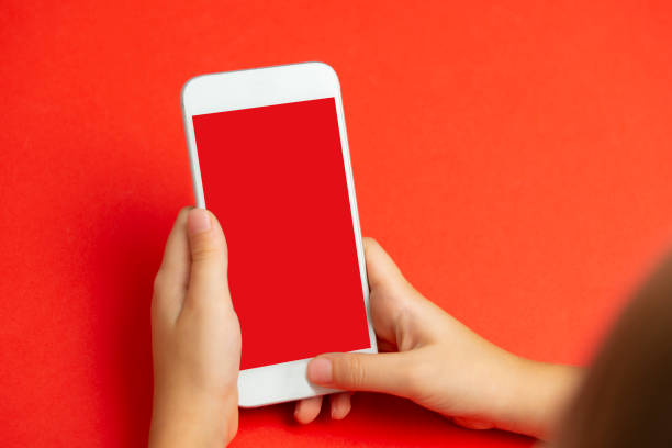 Child using mobile phone. Looking at mobile app, mobile web or game. Phone display is a red. Redbackground.