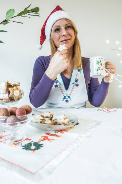 istock Woman Enjoy Christmas Biscuits and Tea in Christmas Hat 1295368055