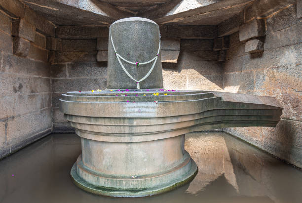 Shivalingam statue at Badavilinga Temple, Hampi, Karnataka, India. Hampi, Karnataka, India - November 5, 2013: Badavilinga Temple. Closeup of massive gray stone monolith statue of Shivalingam symbol standing in water in small chamber with open ceiling. lingam yoni stock pictures, royalty-free photos & images