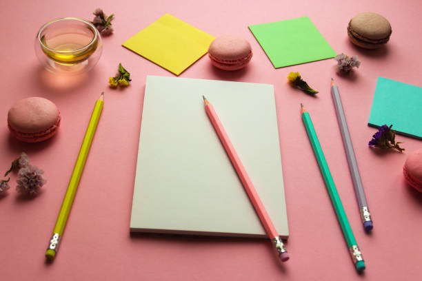 istock Creative feminine workspace with sketchbook for drawing, pencils, a cup of tea and macaroons on pink background. Art concept 1295379811