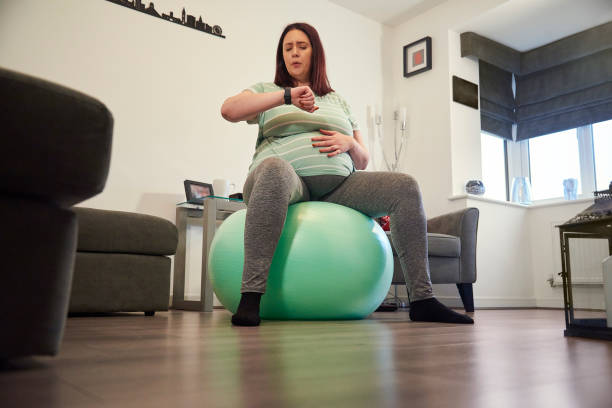 Timing contractions A pregnant lady sat on a gym ball in her living room timing contractions on her watch labor childbirth photos stock pictures, royalty-free photos & images