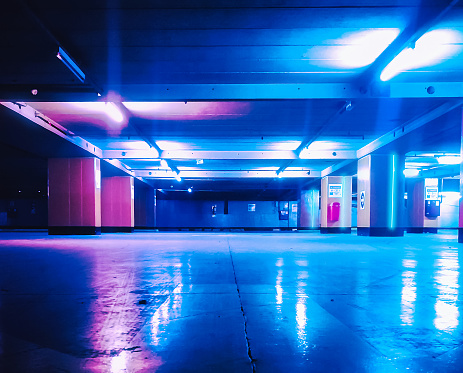 View in perspective of and old and empty parking garage colored with blue-pink tones and artificial neon lights setting a futuristic spaceship atmosphere