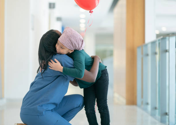 Thank you for being my nurse! A young female cancer patient wearing a headscarf gives her nurse a big hug as they are both at the hallways at the hospital. She is also holding a red balloon that was gifted to her from the hospital staff. cancer cell photos stock pictures, royalty-free photos & images