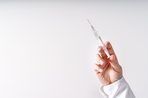 Close up on hand of unknown caucasian woman doctor holding syringe with needle and vaccine injection in front of white wall - covid-19 vaccination concept healthcare and medicine copy space