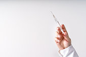 Close up on hand of unknown caucasian woman doctor holding syringe with needle and vaccine injection in front of white wall - covid-19 vaccination concept healthcare and medicine copy space