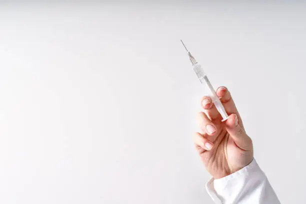 Photo of Close up on hand of unknown caucasian woman doctor holding syringe with needle and vaccine injection in front of white wall - covid-19 vaccination concept healthcare and medicine copy space