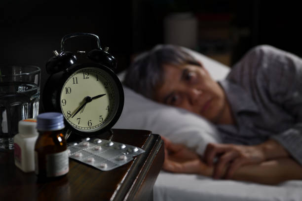 istock A depressed senior woman lying in bed cannot sleep from insomnia. Selective focus on an alarm clock 1295405822