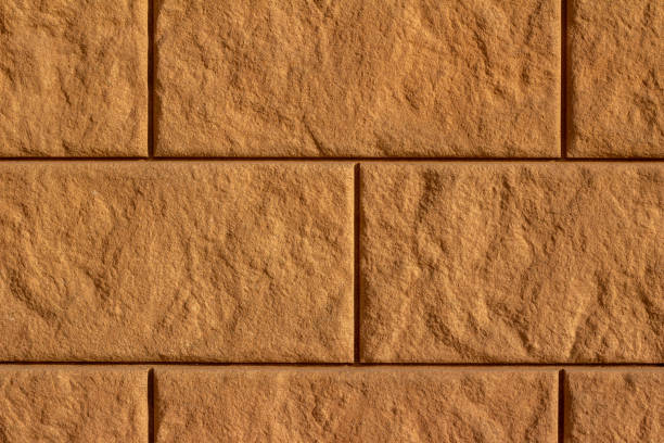 Full frame close-up abstract background of an attractive modern textured brown color large concrete block stone wall in full sunlight.
