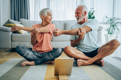 Beautiful mature couple sitting on the floor and practicing yoga. Sporty couple using digital tablet for online yoga lessons.