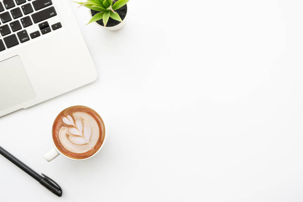 istock Blank notebook with pen are on top of white office desk table with laptop computer, cup of latte coffee and supplies. Top view with copy space, flat lay. 1295426509