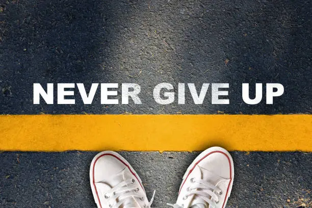 Photo of Never give up written on yellow line on asphalt road