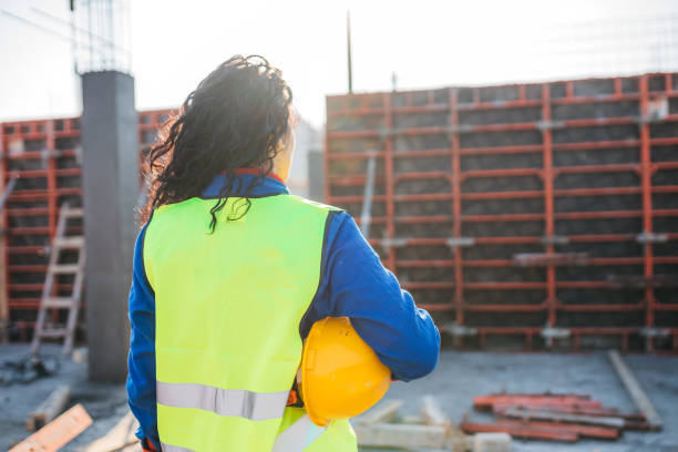 istock Rear view of a female construction contractor on a construction site in a protective hat and hi-vis yellow vest 1295436890