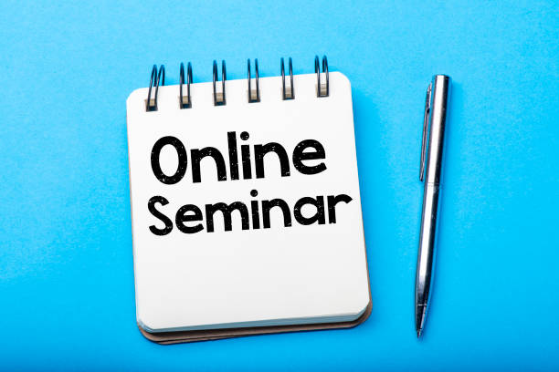 istock ONLINE SEMINAR is written in a white notebook on a blue table 1295437974