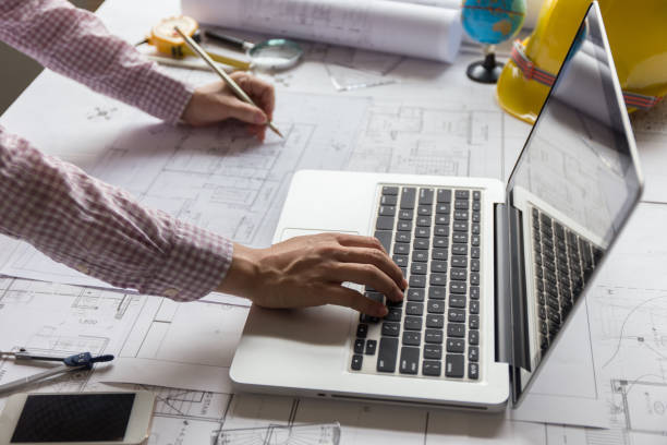 istock Architect working on blueprint and laptop with architect equipments on desk at workplace , side view. 1295440016